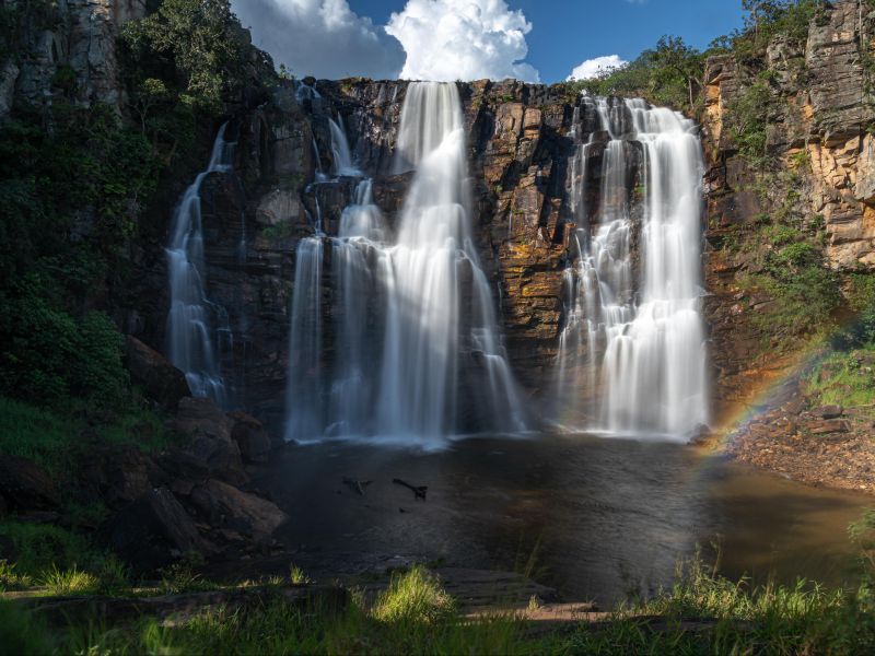 Cachoeira majestosa com arco-íris e vegetação ao redor.