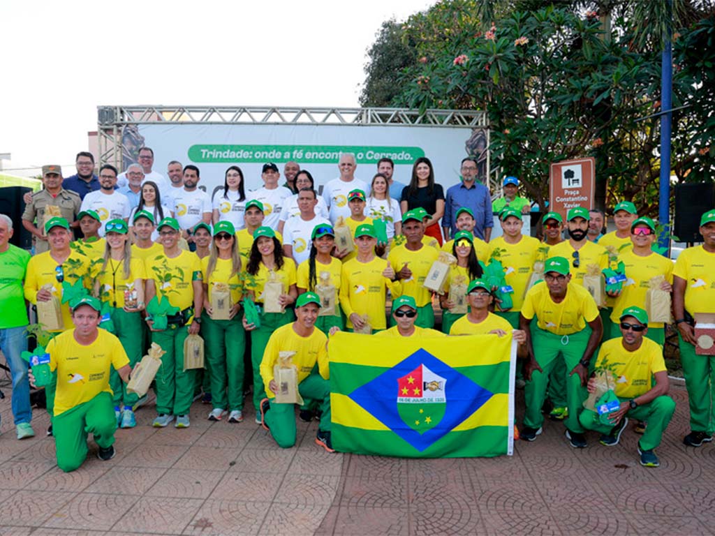 Grupo posando com bandeira e mudas de árvores.