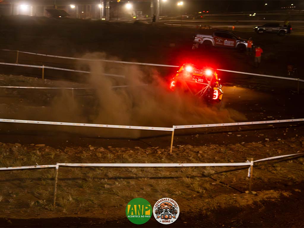 Competição de rally noturno, carro levantando poeira na pista.
