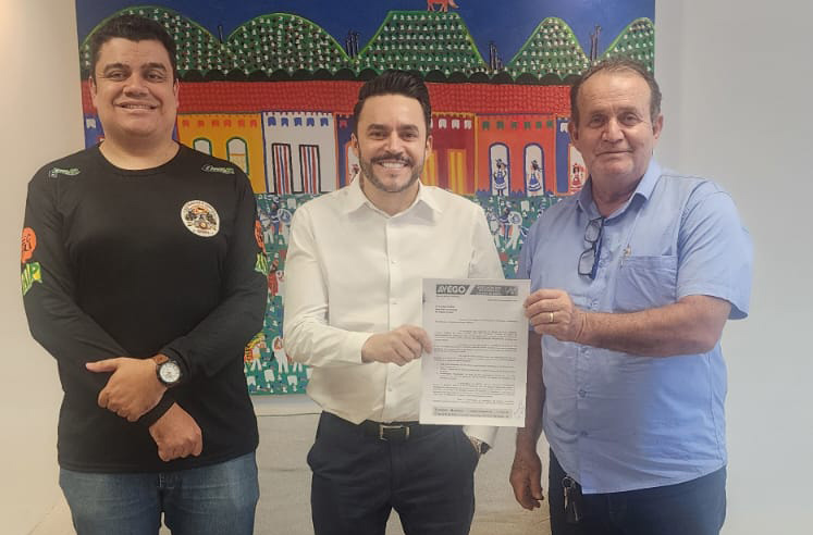 Três homens segurando documento em frente a pintura colorida.