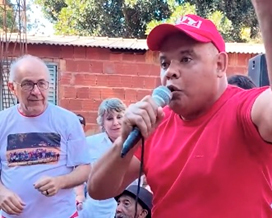 Homem discursando ao microfone em evento ao ar livre.