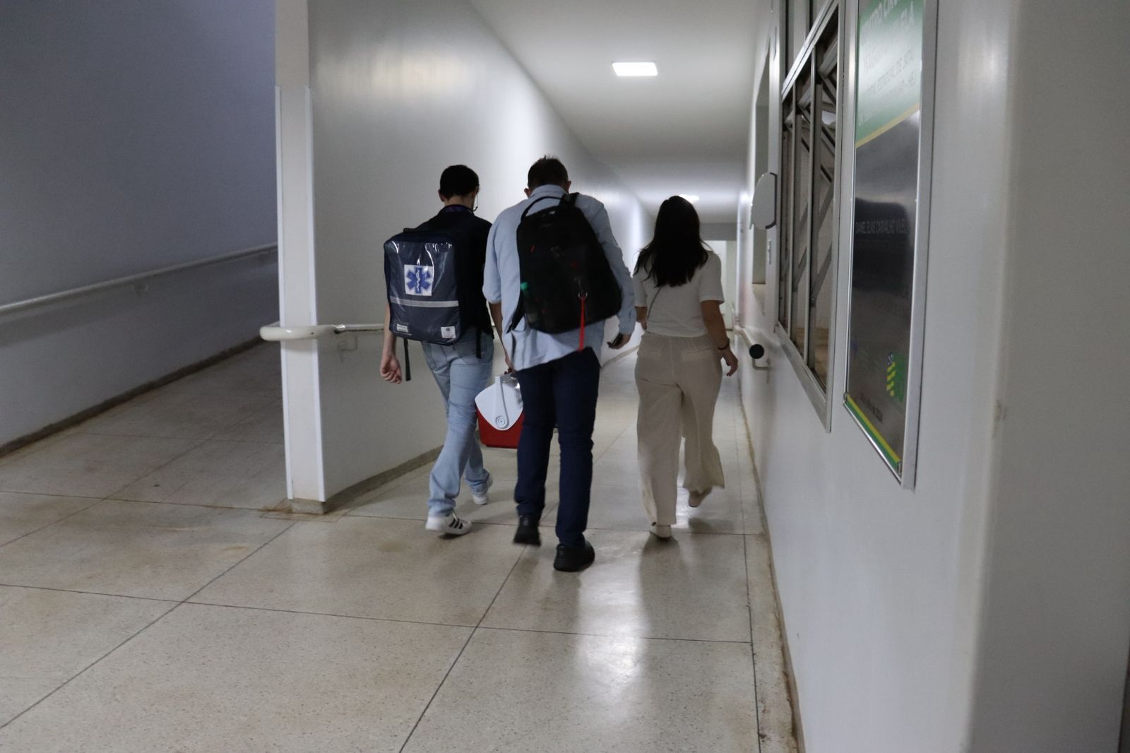 Três pessoas andando em corredor de hospital.