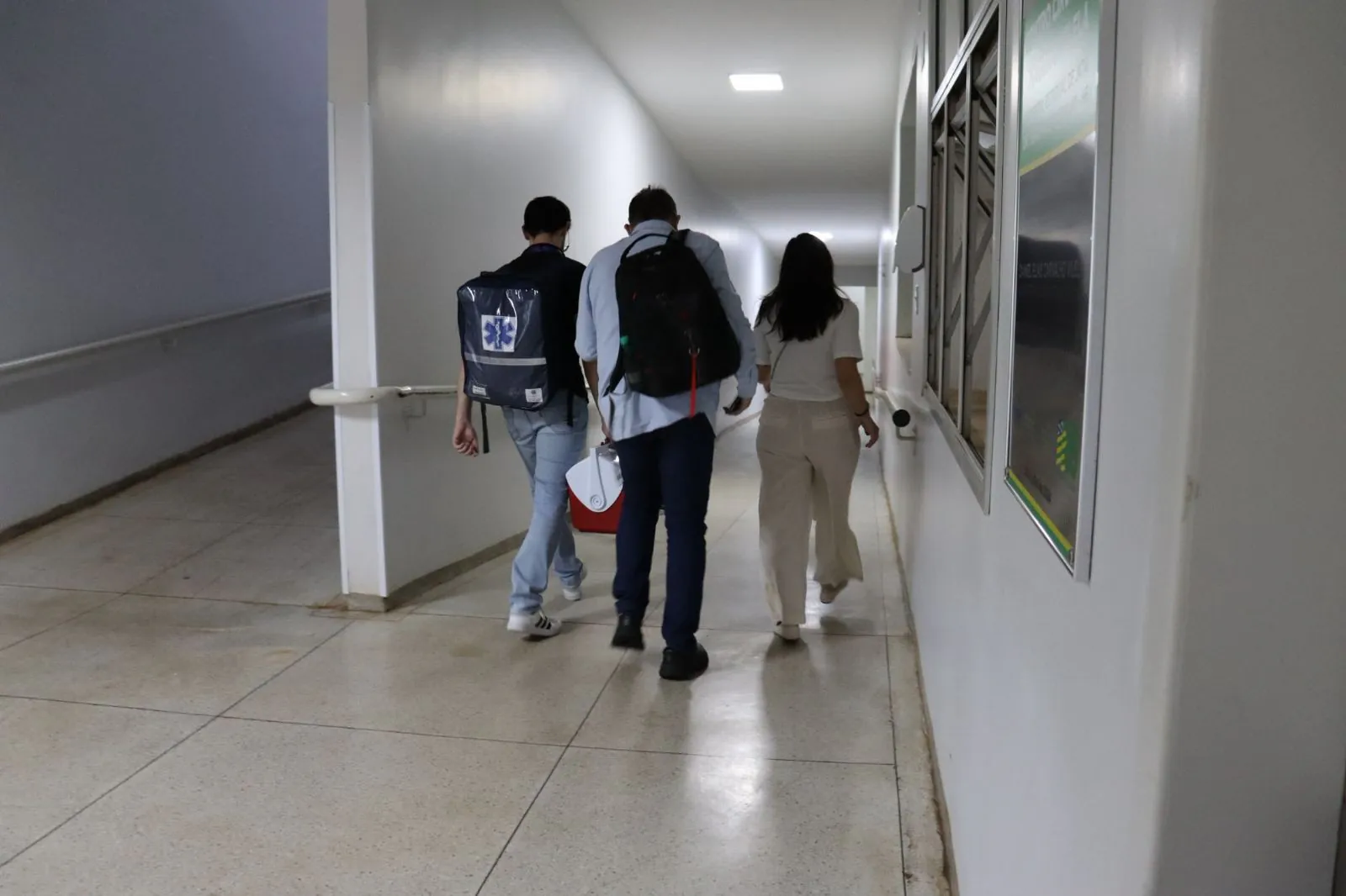 Três pessoas andando em corredor de hospital.