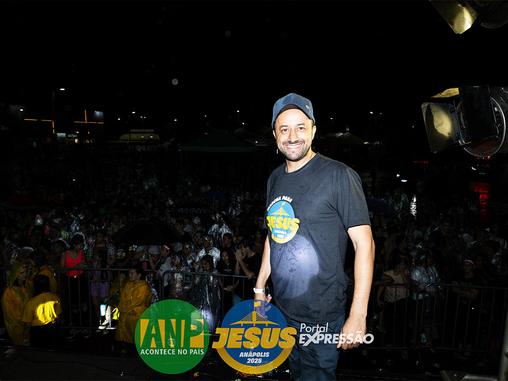 Homem sorrindo em palco durante evento à noite.