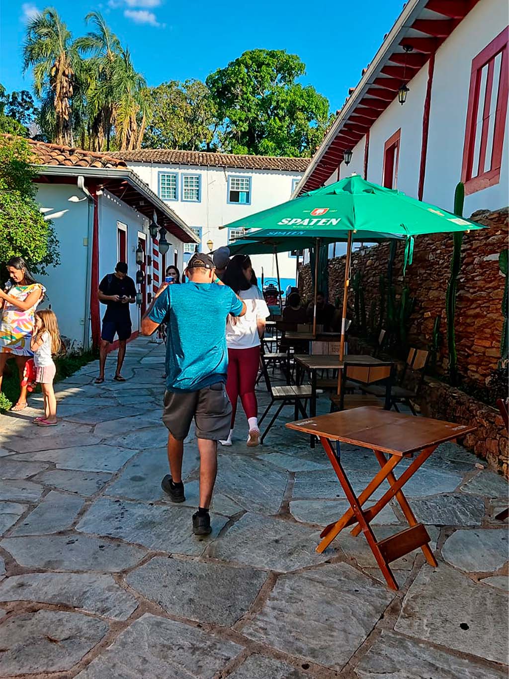 Pessoas andando em pátio com mesas ao ar livre.