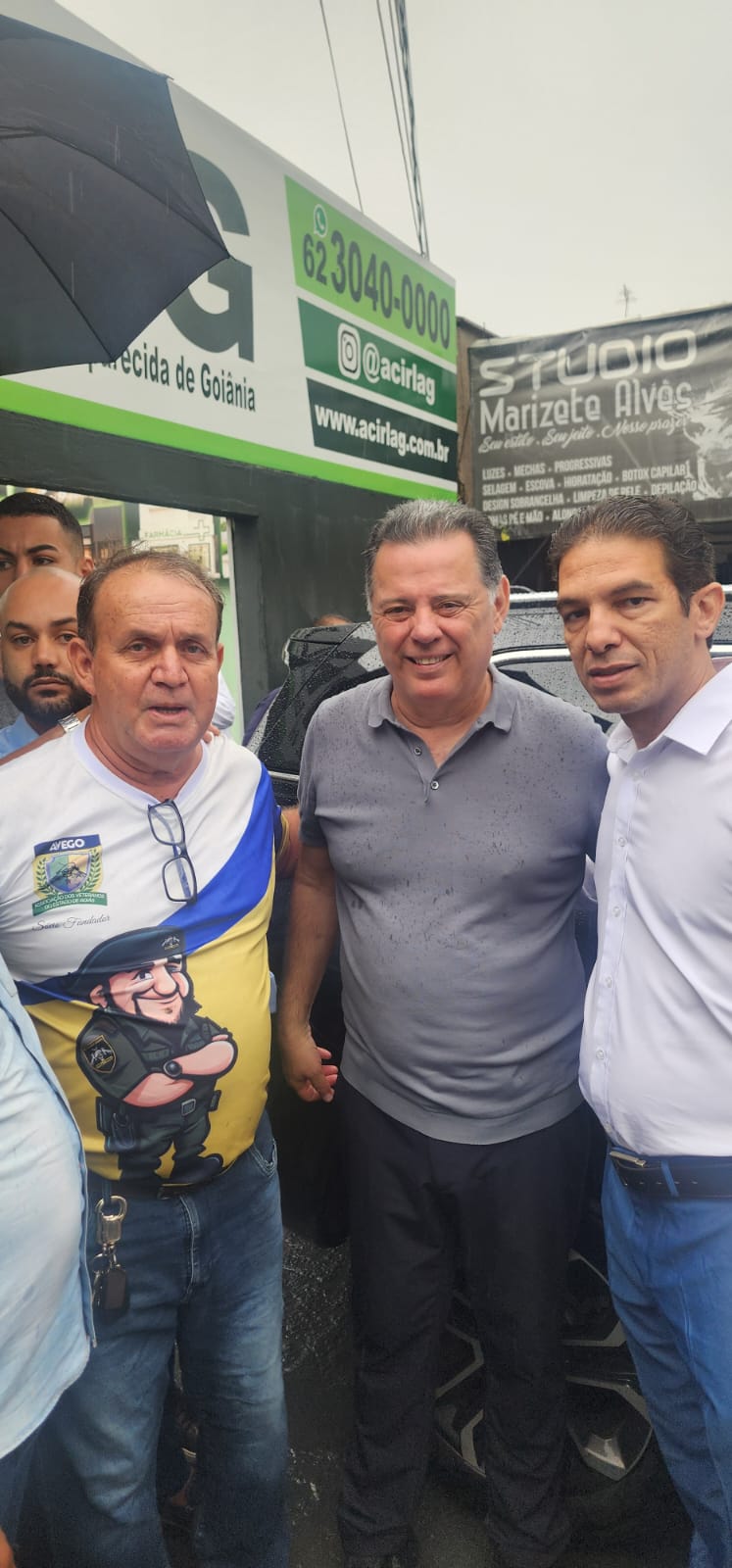 Três homens em frente a placas e anúncio.