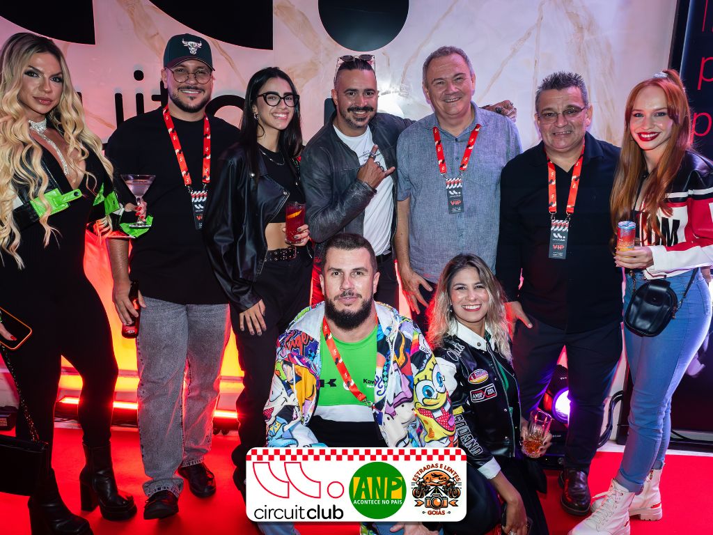 Pessoas posando em evento com crachás e iluminação vermelha.