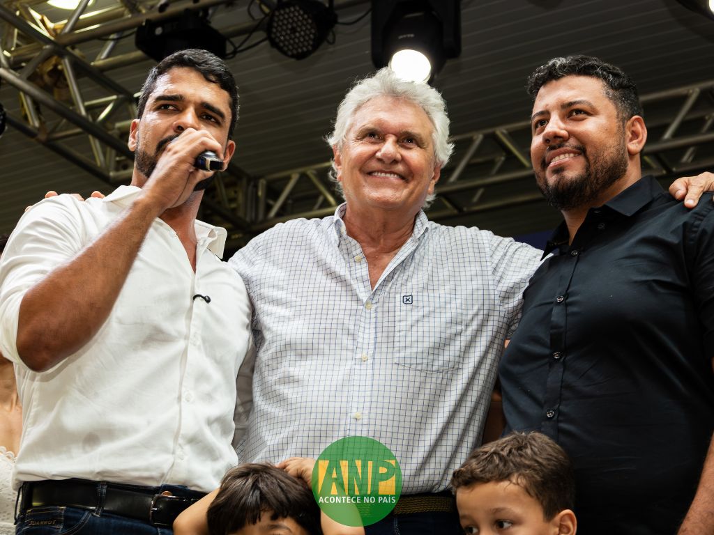 Três homens sorrindo em evento público.