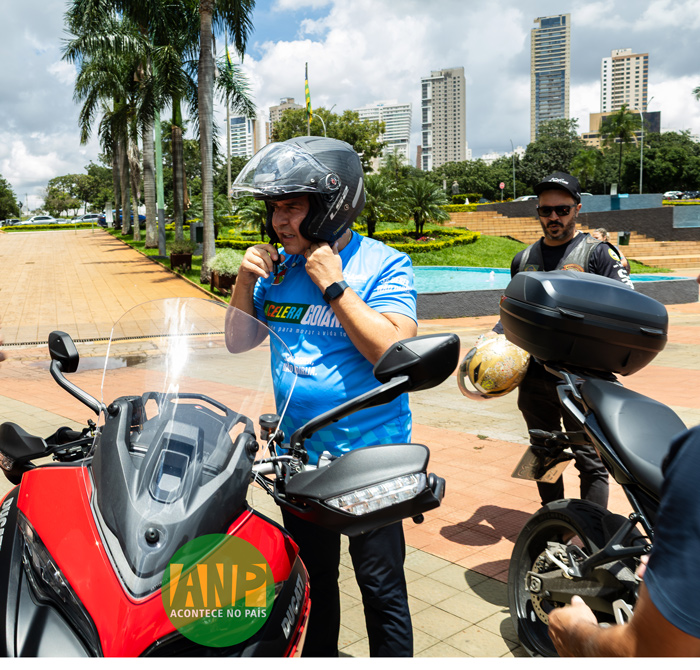 Motociclista ajustando capacete ao lado de motocicleta.