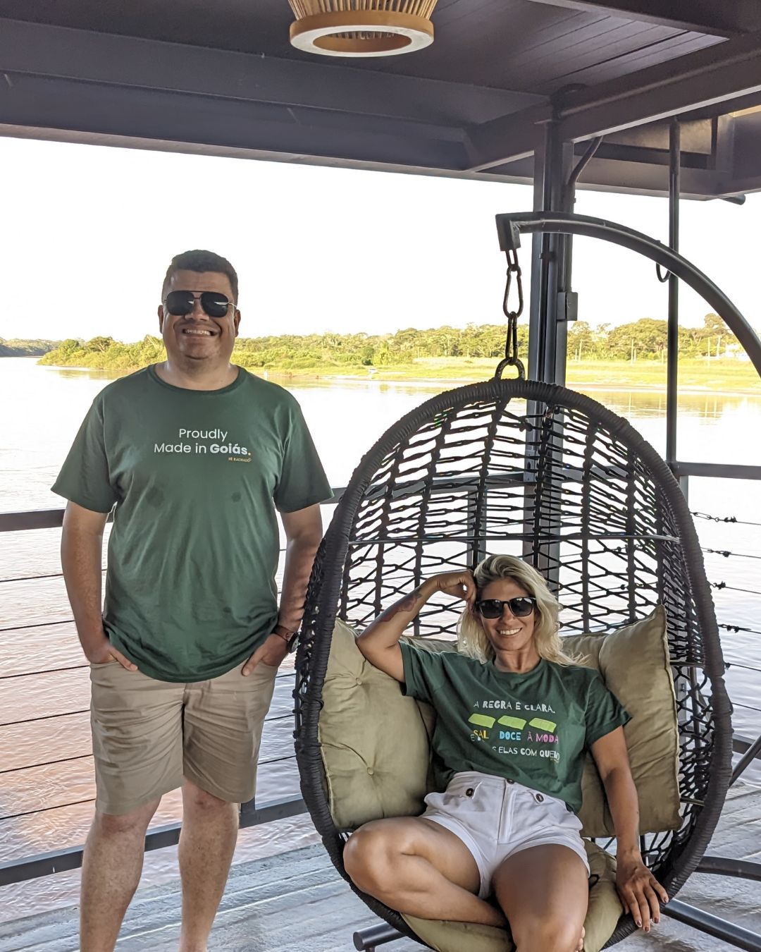 Casal sorrindo na varanda com vista para o rio.