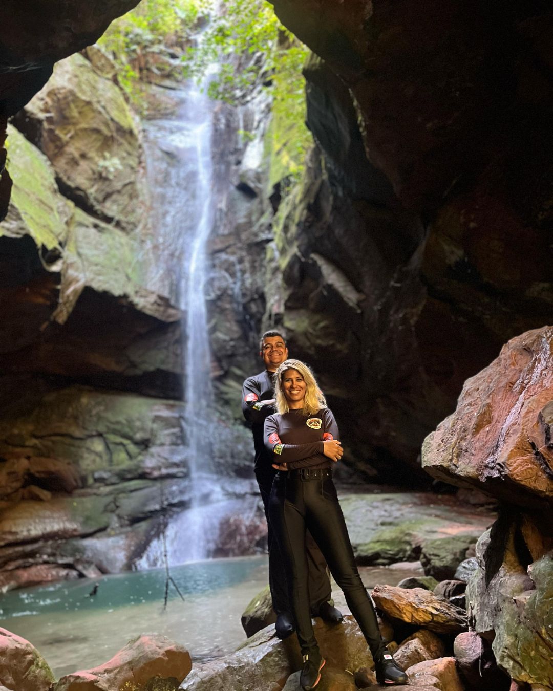 Cachoeira em caverna com duas pessoas sorrindo.