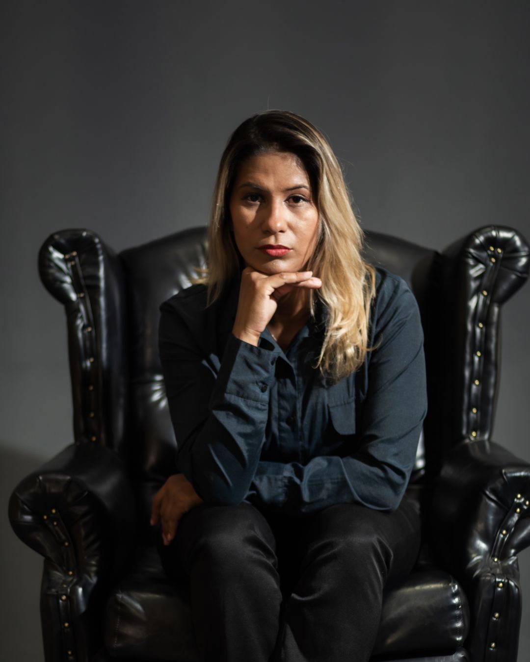 Mulher sentada em poltrona preta, olhar sério.