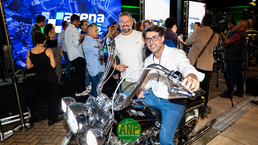 Homem sorrindo em uma motocicleta em evento.