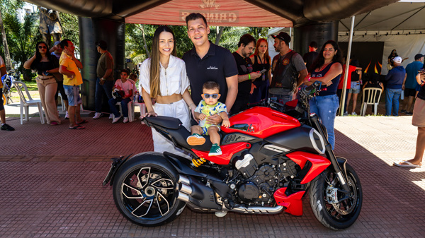 Família posa com moto vermelha em evento ao ar livre.