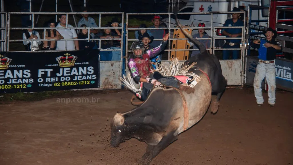 Peão montando touro em rodeio à noite.