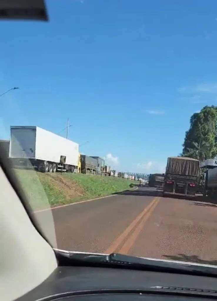 Estrada com fila de caminhões sob céu azul.