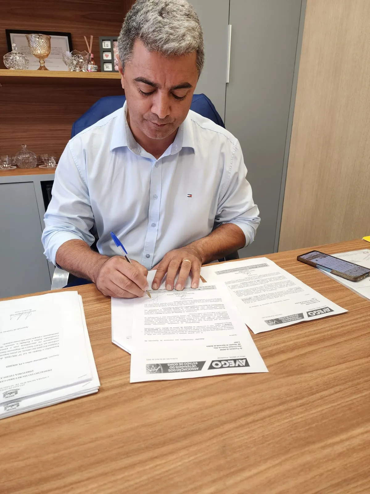 Homem assina documentos em mesa de trabalho.