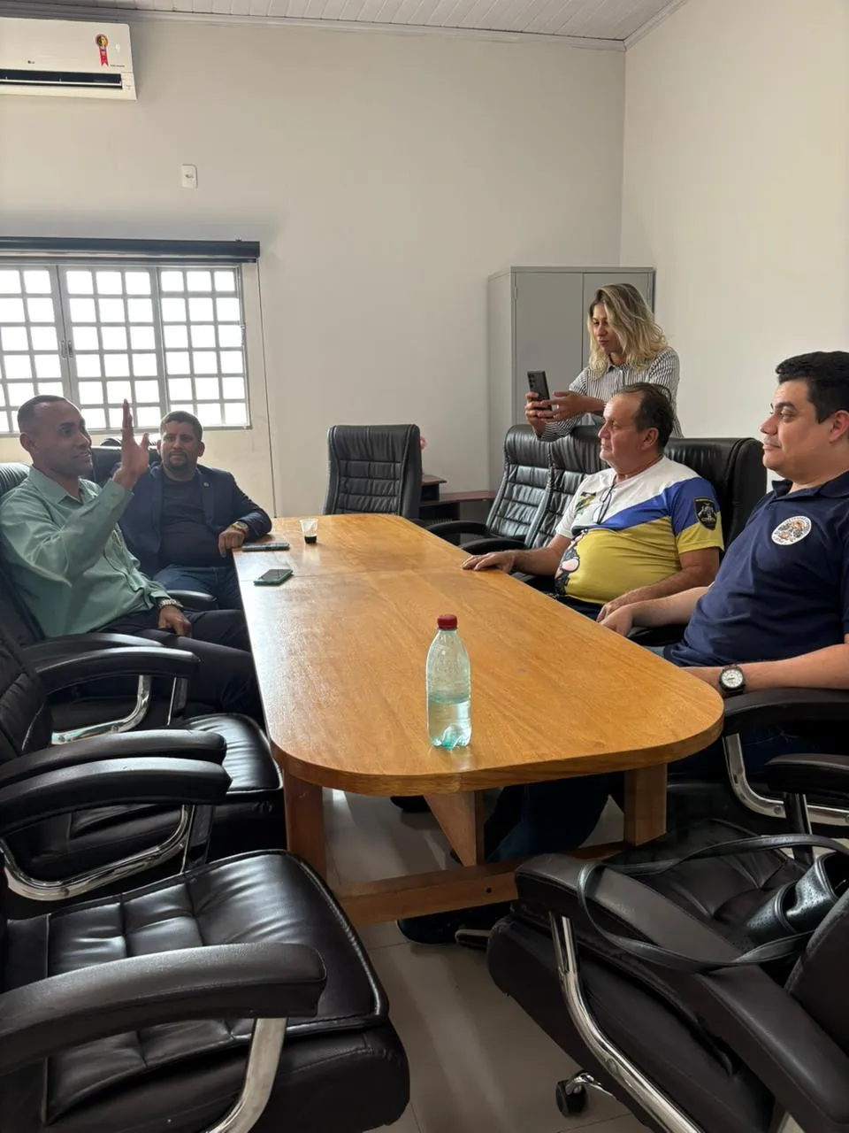 Reunião em sala com mesa de madeira, cinco pessoas.